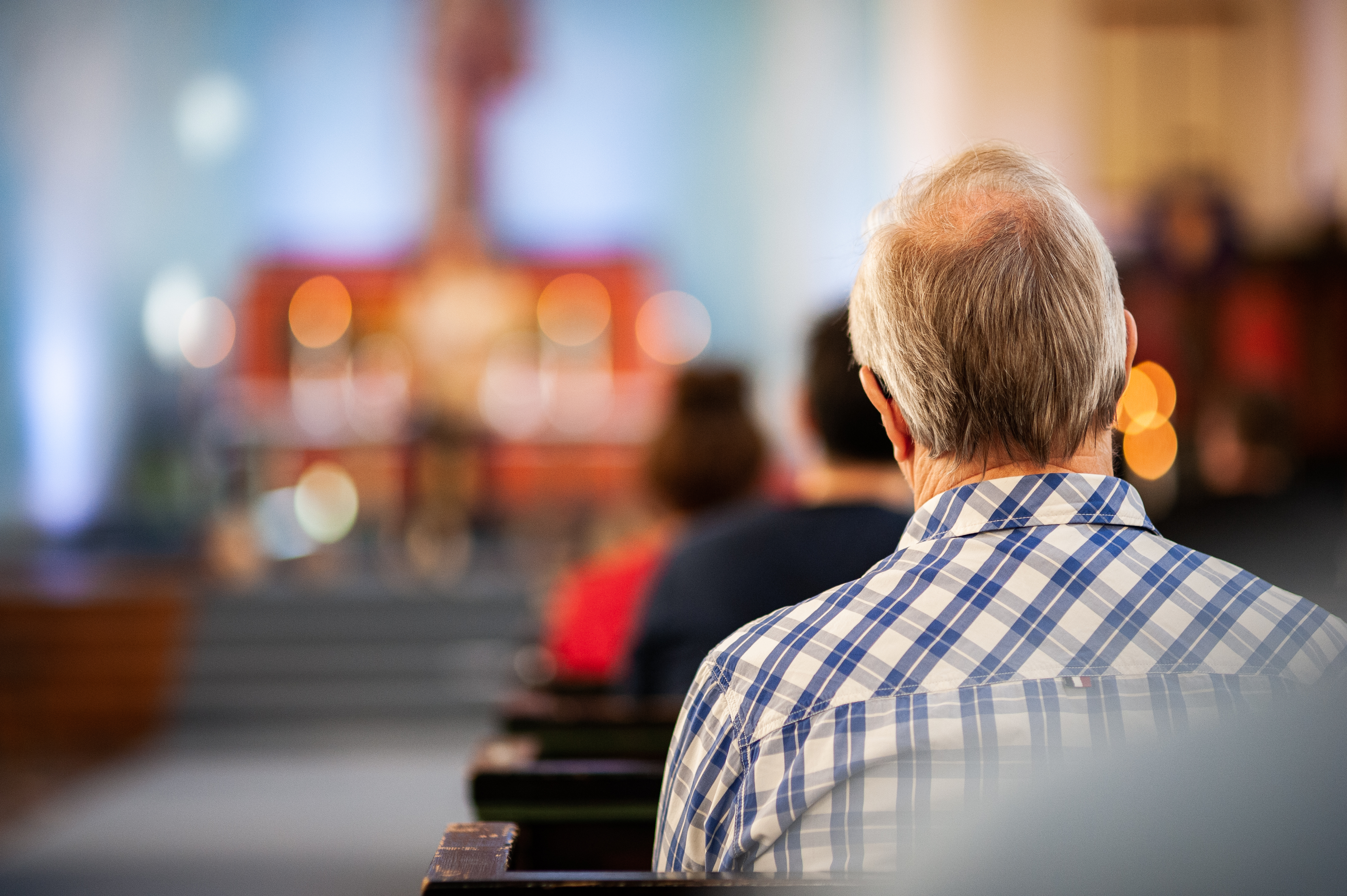 Bildet viser en mann i en kirkebenk som ser mot alteret